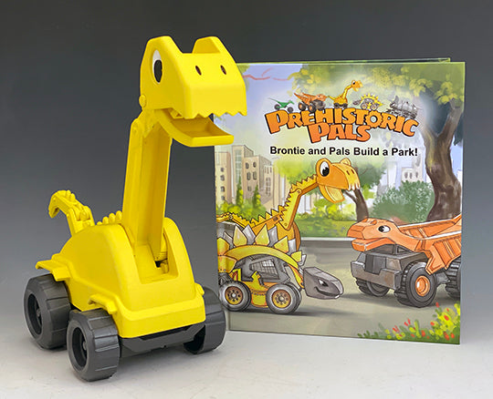This front view of Brontie the dinosaur excavator toy is show with the children's book he is features in.  Brontie and Pals Build a Park. This is the first edition hard cover book with the characters that are a fusion of a vehicle and a dinosaur.  